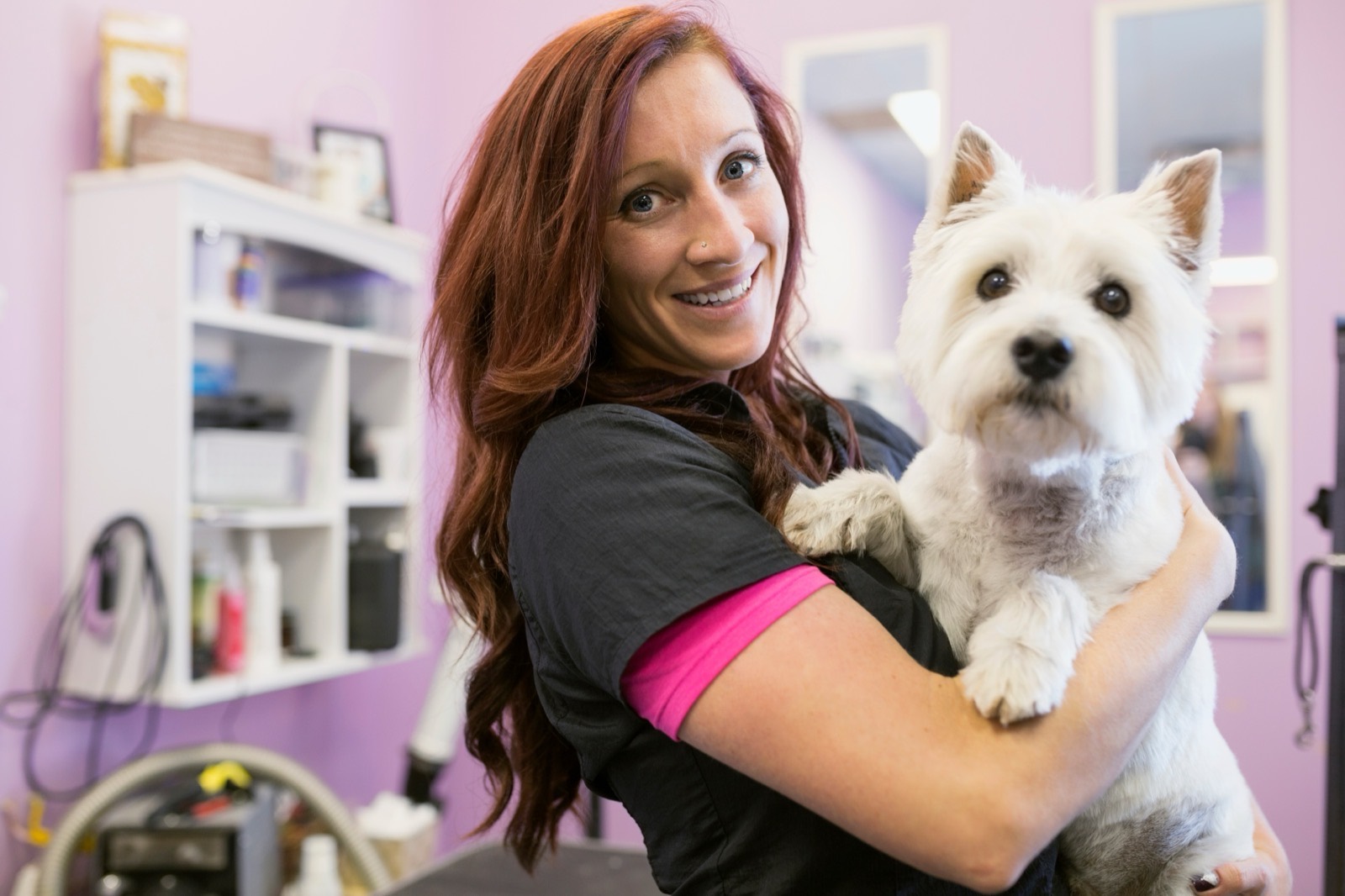 Priya, a Paws & Suds groomer, smiling with a dog